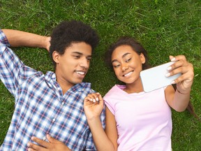 African american teenage couple making selfie while laying on grass, panorama