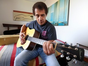 Bienné Blémur sits on a bed playing guitar