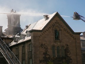 Firefighters at the end of a ladder truck spray the roof of a burning building