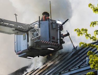 Firefighters at the end of a ladder truck combat a blaze on the roof of an old building