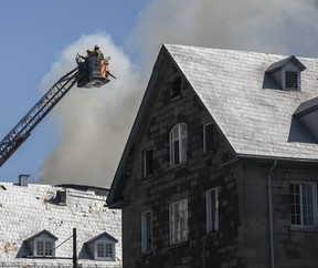 Firefighters at the end of a ladder truck combat a blaze on the roof of an old building