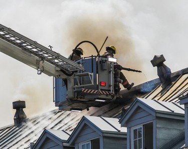 Firefighters at the end of a ladder truck combat a blaze on the roof of an old building