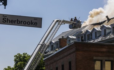 Firefighters at the end of a ladder truck spray the roof of a burning building