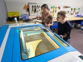 A laser cutter is in the foreground, with a woman and man watching its progress