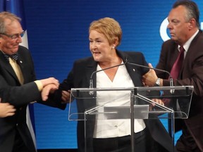 Pauline Marois is grabbed by plainclothes security guards behind a podium on stage