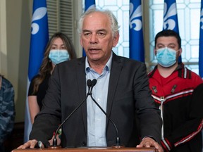 A man speaks at a podium in front of a row of Quebec Flags. Two women are standing behind him.