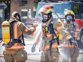 A montreal firefighter is decontaminated with a hose and brush by two firefighters