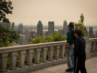 two people look at montreal's skyline which is covered in smog from forest fires