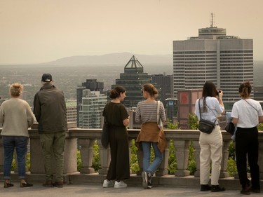 People look at the hazy Montreal skyline from a lookout