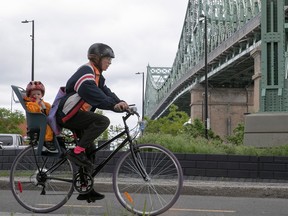 a cyclist with a child in a seat on the back of the bike with the champlain bridge in the background