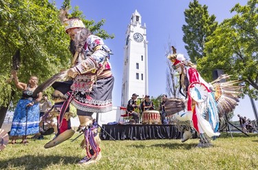Two people in traditional dress dance in front of a clock tower