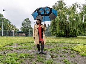 Gracia Kasoki Katahwa in the middle of a park, wearing black rain boots and holding a blue umbrella