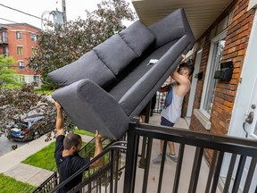 two men carry a grey sofa up stairs into a rowhouse
