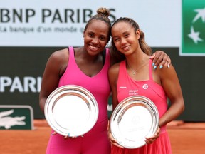 Two female tennis players hold silver plates after a match on a clay court