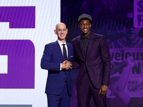A basketball prospect wearing purple greets the NBA commissioner on stage at the draft