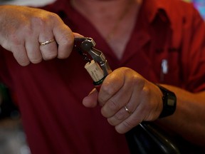 ALCALA DE LOS GAZULES, SPAIN - JULY 02: A waiter removes the cork from a bottle of wine at a bar on July 2, 2013 in Alcala de los Gazules, Spain. Spain and Portugal are the largest producers of cork in the world with Los Alcornocales Natural Park in the Iberian Peninsula being the leading region for production. The ancient cork cultivated in these oak forests is a major world export, financially benefitting the region. The bark from the oak is harvested every nine years, through traditional methods. The best planks are sourced for wine bottling corks while the rest is processed into agglomerate cork.