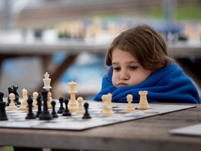 A girl wrapped in a blanket looks at a chess board and puffs her cheeks