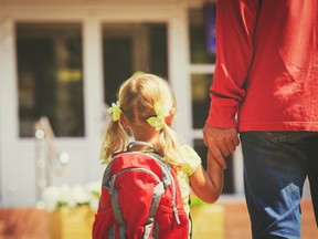a young girl with blond pigtails with a red backpack holds her father's hand