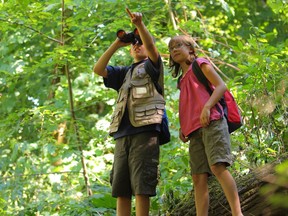 Two children in woods looking through binoculars