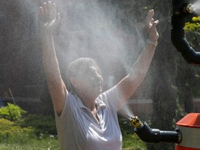 a woman in a light shirt with her arms raised being sprayed by water at a cooling station