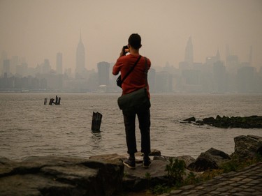 a man in a red shirt takes a photo of the smoky new york skyline