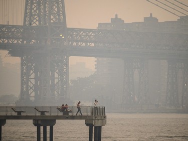 people standing on a new york pier with a smog-covered bridge in the background