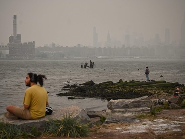 a man in a yellow shirt sits on a rock with a hazy new york skyline in the background