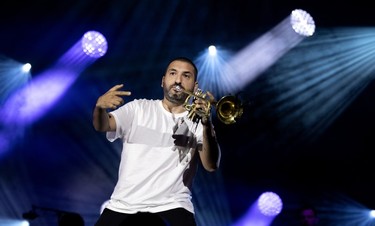A man gestures with one hand while playing the trumpet on stage