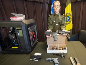 A female police officer holds a 3D printed gun above a table with other such items and a 3D printer