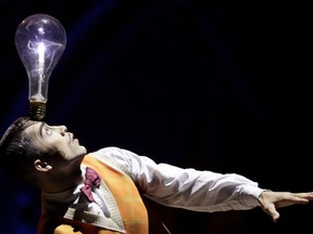 a cirque du soleil performer balances a large lit lightbulb on his head