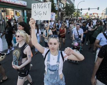 A woman gives the thumbs down gesture while holding a sign that reads "angry sign" during a march