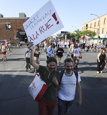 A man holds a "Legault, Duranceeau à la rue!" sign during a march