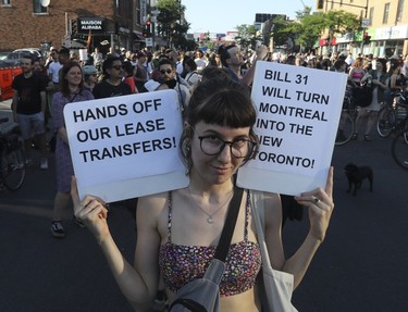 A woman holds signs reading "hands off our lease transfers!" and "Bill 31 will turn Montreal into the new Toronto!" at a march