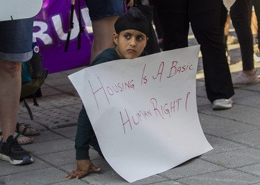 A seated boy holds a "housing is a basic human right!" sign at a protest