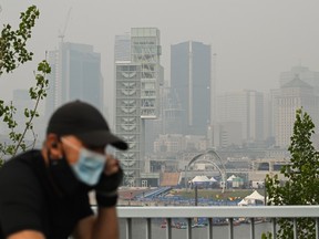A man wears a face mask as he cycles by the skyline of Montreal, on Sunday, June 25, 2023. A smog warning is in effect for Montreal and multiple regions of the province because of forest fires.