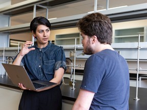 A photo of two people, one of whom is holding a laptop, talking in a research lab