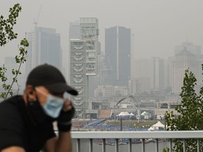 Environment Canada says forest fires are causing poor air quality across much of Quebec and Ontario. A man wears a face mask as he cycles by the skyline of Montreal on June 25, 2023.