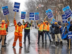 Striking workers in orange safety gear hold signs as they stand in a street