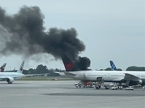Smokes billows from a vehicle on fire underneath a plane on the tarmac