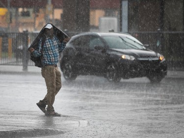 A man uses his jacket to cover his head as Heavy rain falls on a street