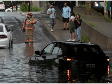 Montreal firefighters look over scene of people waiting near their flooded car at Gince St. under Highway 15 after the underpass flooded following heavy rain storm in Montreal on Thursday July 13, 2023.