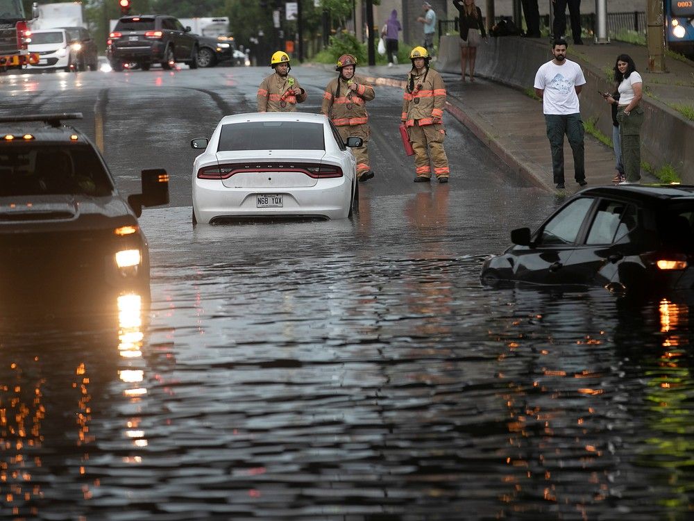 Montreal firefighters look over scene of people waiting near their flooded car at Gince St. under Highway 15 after the underpass flooded following heavy rain storm in Montreal on Thursday July 13, 2023.