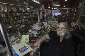 A man sits at the cash, surrounded by piles of books, in a closed bookstore