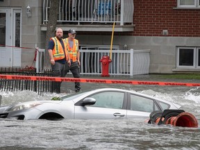 city workers on a sidewalk next to a flooded street with submerged cars