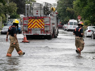 firefighters walk on flooded street with fire truck in the background