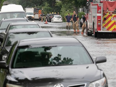firefighters look at submerged street and cars after a water main break