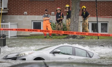 firefighters organize next to a flooded street and submerged car