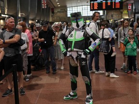 a person dressed as a REM superhero stands in a crowd of commuters