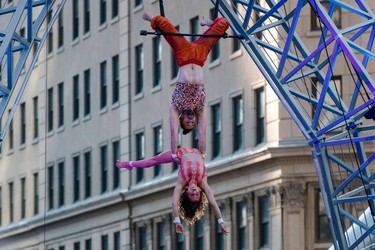 Two aerial acrobats swing upside down from a small bar