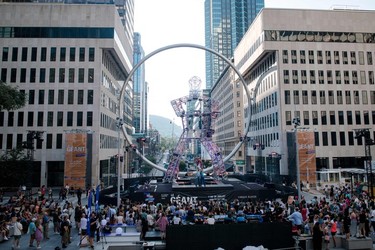 A crowd watches a circus performance on a stage with a giant robot structure between two office towers